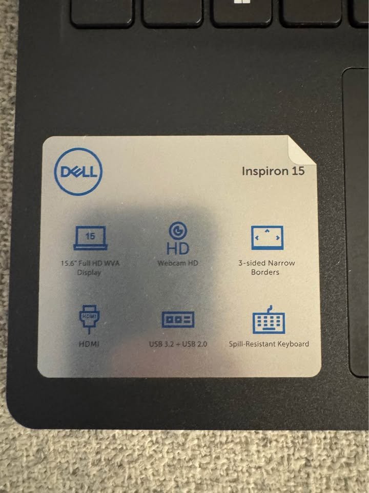 Close-up of Dell Inspiron 15 specification label confirming display size, ports, HD webcam, and spill-resistant keyboard