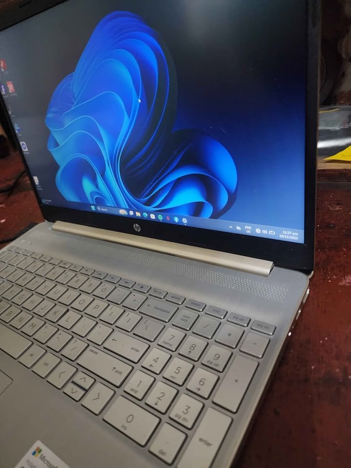 Close-up of HP 15 laptop keyboard with full-size numeric keypad on silver chassis, Windows 11 screen in background