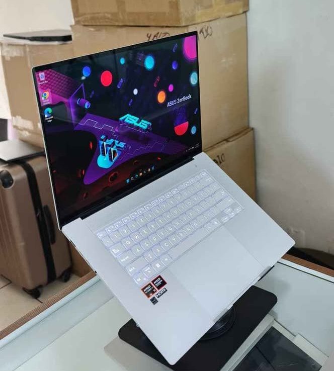 ASUS ZenBook S 16 laptop in Ceramic White color displayed on a stand showing the AMD-powered slim laptop